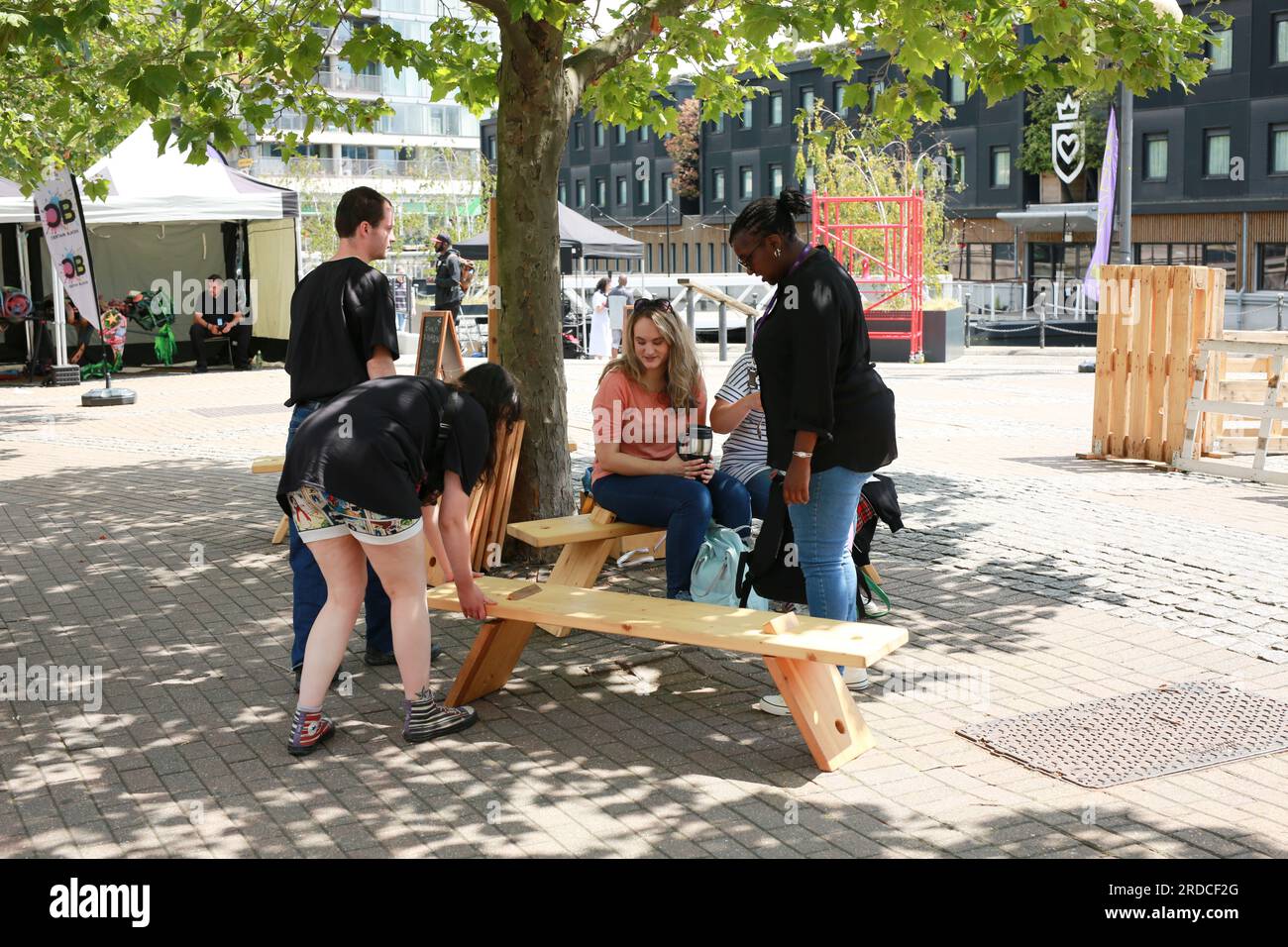 Londres, Royaume-Uni. 20 juillet 2023. 'Bench invasion' de la Compagnie Krak. Dans la performance 'Bench invasion', l'artiste belge Dieter Peter Raphaël Missiaen se déplace dans l'espace public avec dix personnes locales, chacune avec un banc sous le bras, à la recherche de contacts. À un moment inopiné, ils installent des bancs et invitent activement les gens à s’asseoir devant eux. De cette façon, il (re)connecte les gens. Le Festival d'ensemble est un festival de quatre jours de théâtre, de cirque, de danse, de musique et d'art numérique gratuits au Royal Victoria Dock. Ensemble Festival explore les thèmes de l'écologie, de la vie moderne et de la reconnexion, et comprend deux jours de pop-up per Banque D'Images