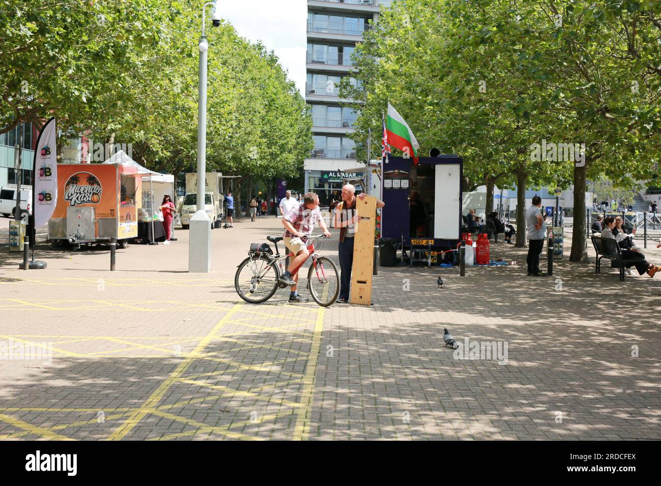 Londres, Royaume-Uni. 20 juillet 2023. 'Bench invasion' de la Compagnie Krak. Dans la performance 'Bench invasion', l'artiste belge Dieter Peter Raphaël Missiaen se déplace dans l'espace public avec dix personnes locales, chacune avec un banc sous le bras, à la recherche de contacts. À un moment inopiné, ils installent des bancs et invitent activement les gens à s’asseoir devant eux. De cette façon, il (re)connecte les gens. Le Festival d'ensemble est un festival de quatre jours de théâtre, de cirque, de danse, de musique et d'art numérique gratuits au Royal Victoria Dock. Ensemble Festival explore les thèmes de l'écologie, de la vie moderne et de la reconnexion, et comprend deux jours de pop-up per Banque D'Images