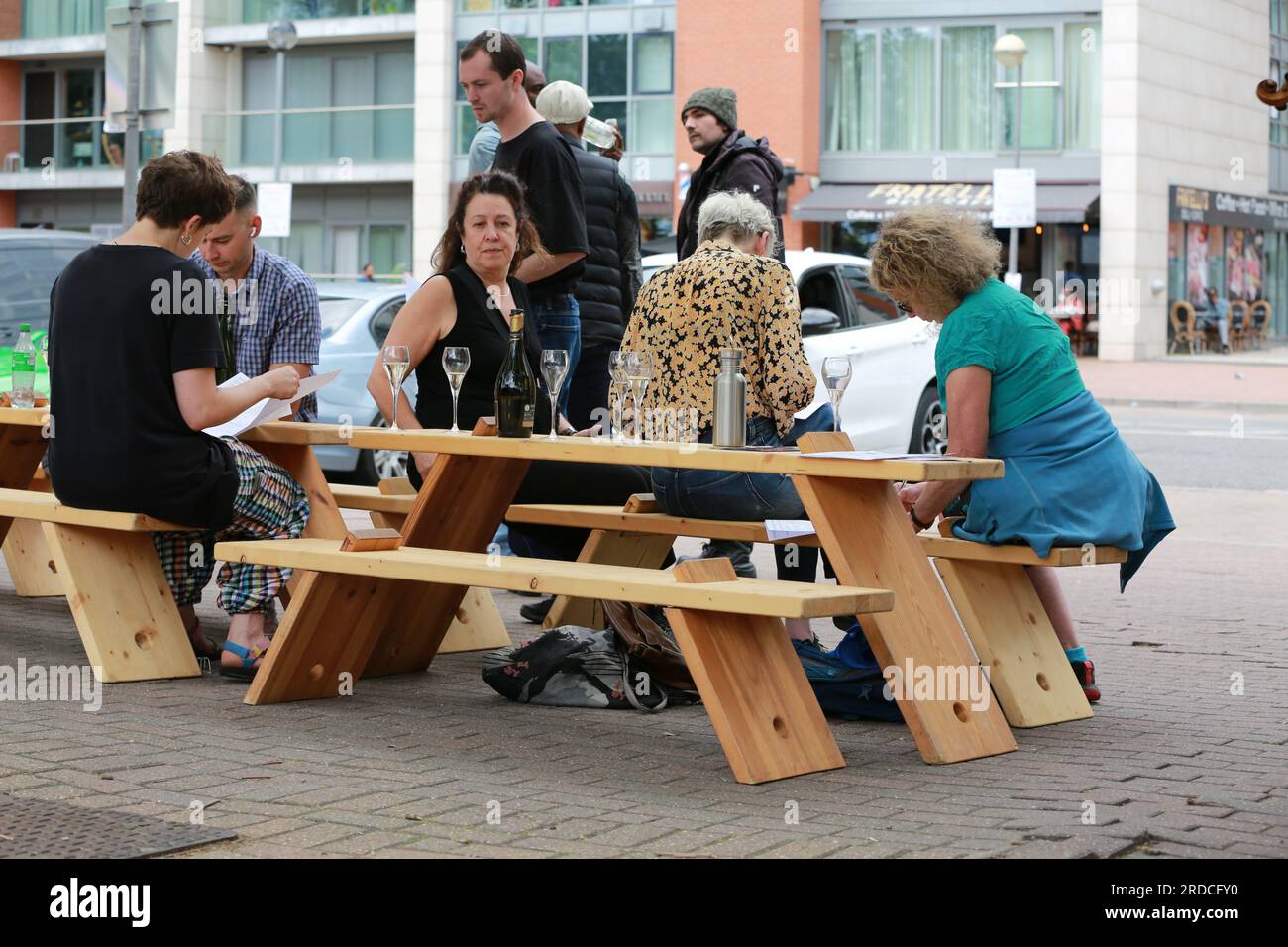 Londres, Royaume-Uni. 20 juillet 2023. 'Bench invasion' de la Compagnie Krak. Dans la performance 'Bench invasion', l'artiste belge Dieter Peter Raphaël Missiaen se déplace dans l'espace public avec dix personnes locales, chacune avec un banc sous le bras, à la recherche de contacts. À un moment inopiné, ils installent des bancs et invitent activement les gens à s’asseoir devant eux. De cette façon, il (re)connecte les gens. Le Festival d'ensemble est un festival de quatre jours de théâtre, de cirque, de danse, de musique et d'art numérique gratuits au Royal Victoria Dock. Ensemble Festival explore les thèmes de l'écologie, de la vie moderne et de la reconnexion, et comprend deux jours de pop-up per Banque D'Images