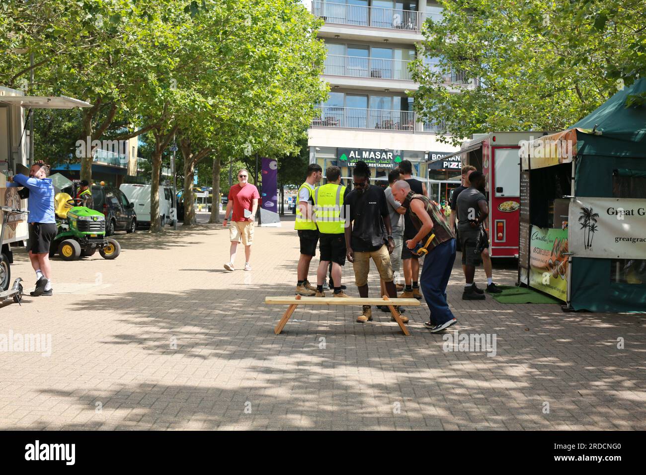 Londres, Royaume-Uni. 20 juillet 2023. 'Bench invasion' de la Compagnie Krak. Dans la performance 'Bench invasion', l'artiste belge Dieter Peter Raphaël Missiaen se déplace dans l'espace public avec dix personnes locales, chacune avec un banc sous le bras, à la recherche de contacts. À un moment inopiné, ils installent des bancs et invitent activement les gens à s’asseoir devant eux. De cette façon, il (re)connecte les gens. Le Festival d'ensemble est un festival de quatre jours de théâtre, de cirque, de danse, de musique et d'art numérique gratuits au Royal Victoria Dock. Ensemble Festival explore les thèmes de l'écologie, de la vie moderne et de la reconnexion, et comprend deux jours de pop-up per Banque D'Images
