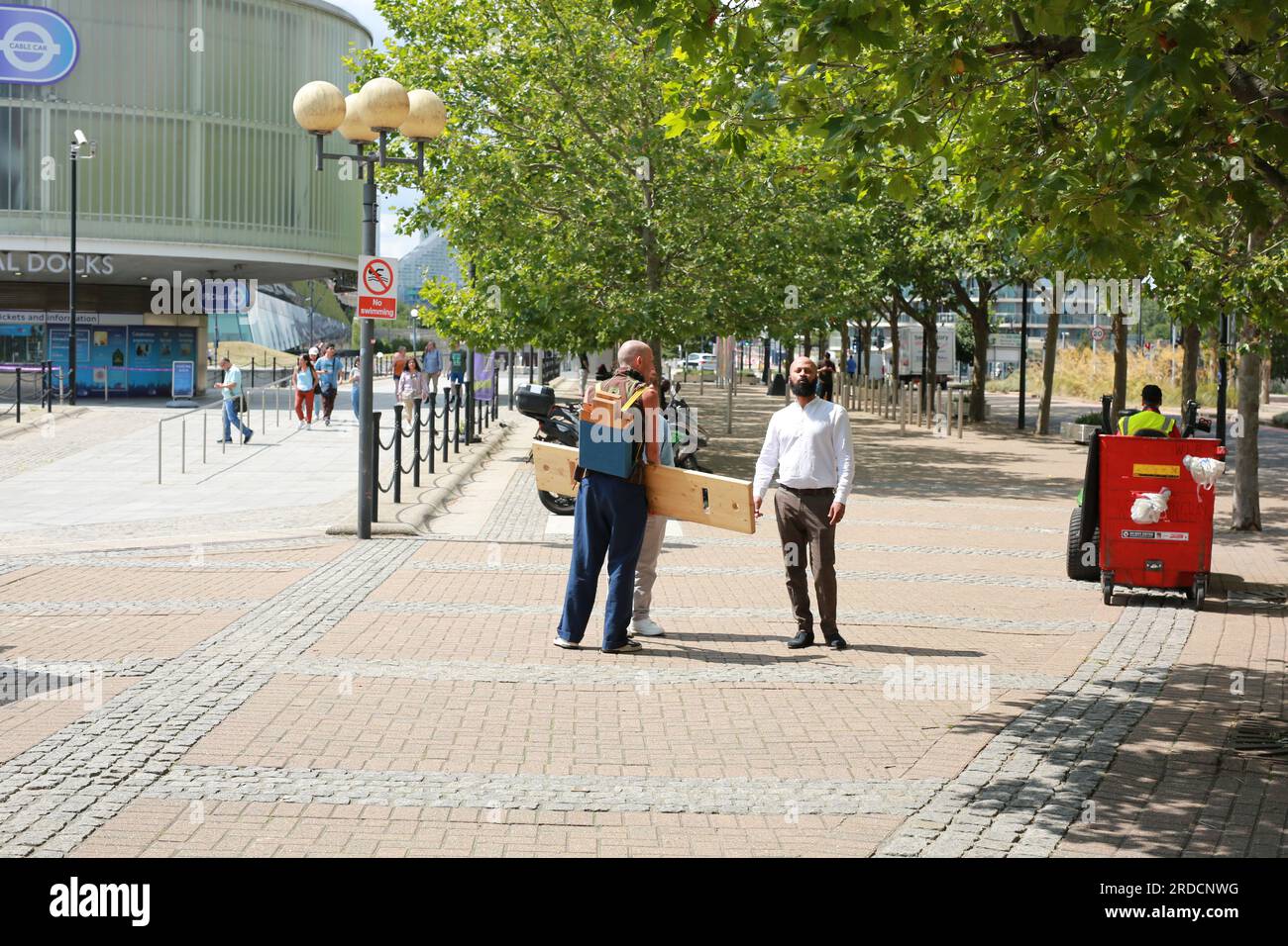 Londres, Royaume-Uni. 20 juillet 2023. 'Bench invasion' de la Compagnie Krak. Dans la performance 'Bench invasion', l'artiste belge Dieter Peter Raphaël Missiaen se déplace dans l'espace public avec dix personnes locales, chacune avec un banc sous le bras, à la recherche de contacts. À un moment inopiné, ils installent des bancs et invitent activement les gens à s’asseoir devant eux. De cette façon, il (re)connecte les gens. Le Festival d'ensemble est un festival de quatre jours de théâtre, de cirque, de danse, de musique et d'art numérique gratuits au Royal Victoria Dock. Ensemble Festival explore les thèmes de l'écologie, de la vie moderne et de la reconnexion, et comprend deux jours de pop-up per Banque D'Images