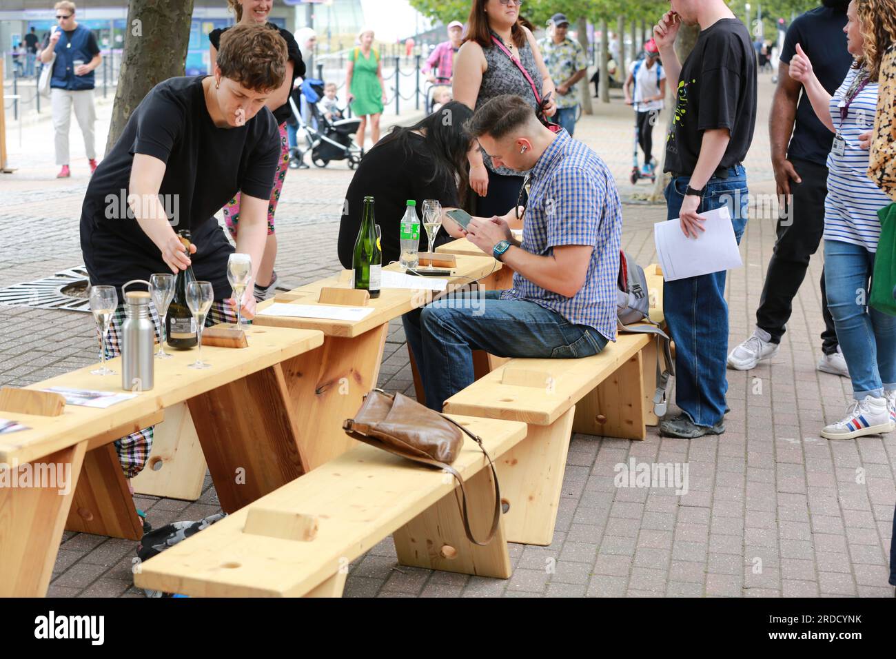 Londres, Royaume-Uni. 20 juillet 2023. 'Bench invasion' de la Compagnie Krak. Dans la performance 'Bench invasion', l'artiste belge Dieter Peter Raphaël Missiaen se déplace dans l'espace public avec dix personnes locales, chacune avec un banc sous le bras, à la recherche de contacts. À un moment inopiné, ils installent des bancs et invitent activement les gens à s’asseoir devant eux. De cette façon, il (re)connecte les gens. Le Festival d'ensemble est un festival de quatre jours de théâtre, de cirque, de danse, de musique et d'art numérique gratuits au Royal Victoria Dock. Ensemble Festival explore les thèmes de l'écologie, de la vie moderne et de la reconnexion, et comprend deux jours de pop-up per Banque D'Images