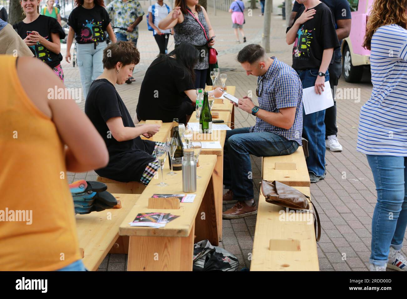 Londres, Royaume-Uni. 20 juillet 2023. 'Bench invasion' de la Compagnie Krak. Dans la performance 'Bench invasion', l'artiste belge Dieter Peter Raphaël Missiaen se déplace dans l'espace public avec dix personnes locales, chacune avec un banc sous le bras, à la recherche de contacts. À un moment inopiné, ils installent des bancs et invitent activement les gens à s’asseoir devant eux. De cette façon, il (re)connecte les gens. Le Festival d'ensemble est un festival de quatre jours de théâtre, de cirque, de danse, de musique et d'art numérique gratuits au Royal Victoria Dock. Ensemble Festival explore les thèmes de l'écologie, de la vie moderne et de la reconnexion, et comprend deux jours de pop-up per Banque D'Images