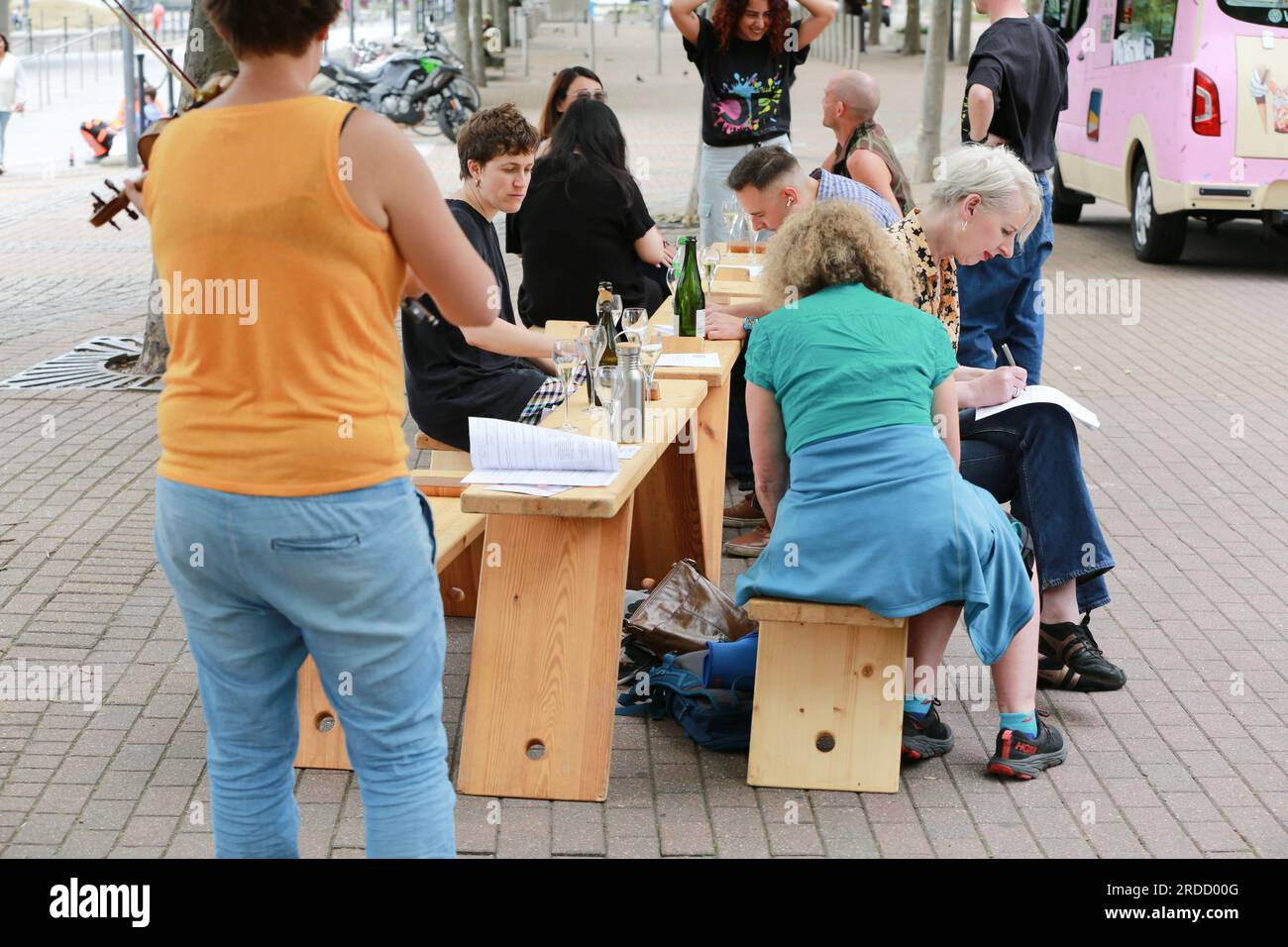 Londres, Royaume-Uni. 20 juillet 2023. 'Bench invasion' de la Compagnie Krak. Dans la performance 'Bench invasion', l'artiste belge Dieter Peter Raphaël Missiaen se déplace dans l'espace public avec dix personnes locales, chacune avec un banc sous le bras, à la recherche de contacts. À un moment inopiné, ils installent des bancs et invitent activement les gens à s’asseoir devant eux. De cette façon, il (re)connecte les gens. Le Festival d'ensemble est un festival de quatre jours de théâtre, de cirque, de danse, de musique et d'art numérique gratuits au Royal Victoria Dock. Ensemble Festival explore les thèmes de l'écologie, de la vie moderne et de la reconnexion, et comprend deux jours de pop-up per Banque D'Images