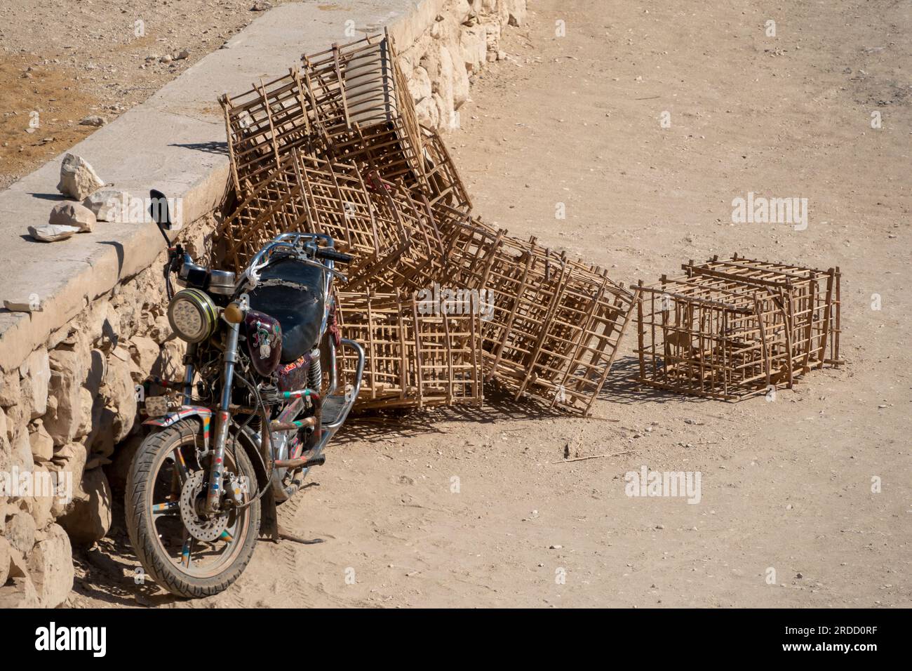 Une moto garée sur le sable près d'un mur de pierre à côté d'une pile de caisses de cannes fendues fabriquées localement Banque D'Images