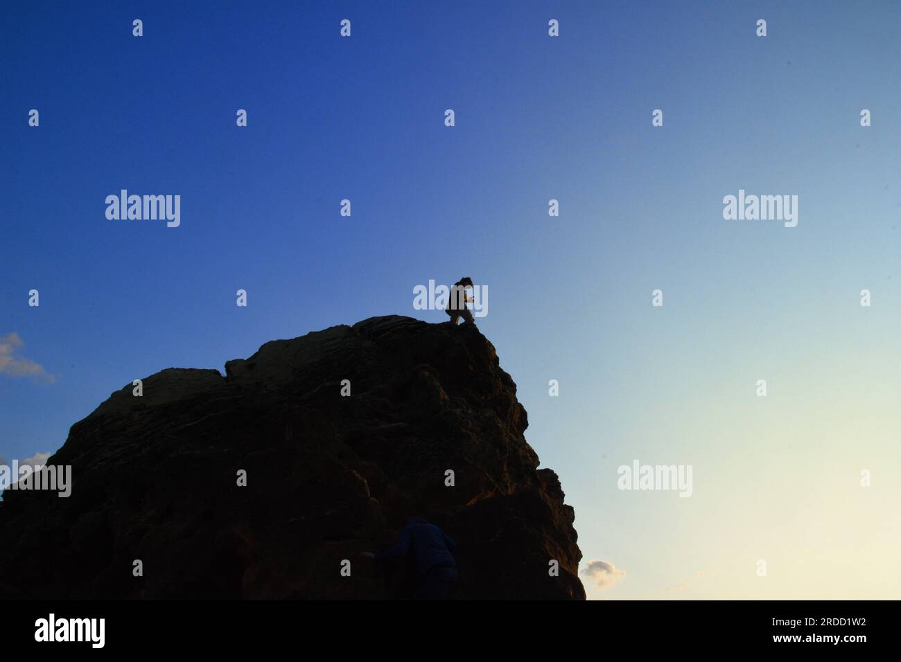 Silhouette d'une jeune personne regardant vers le bas d'un grand rocher. Banque D'Images