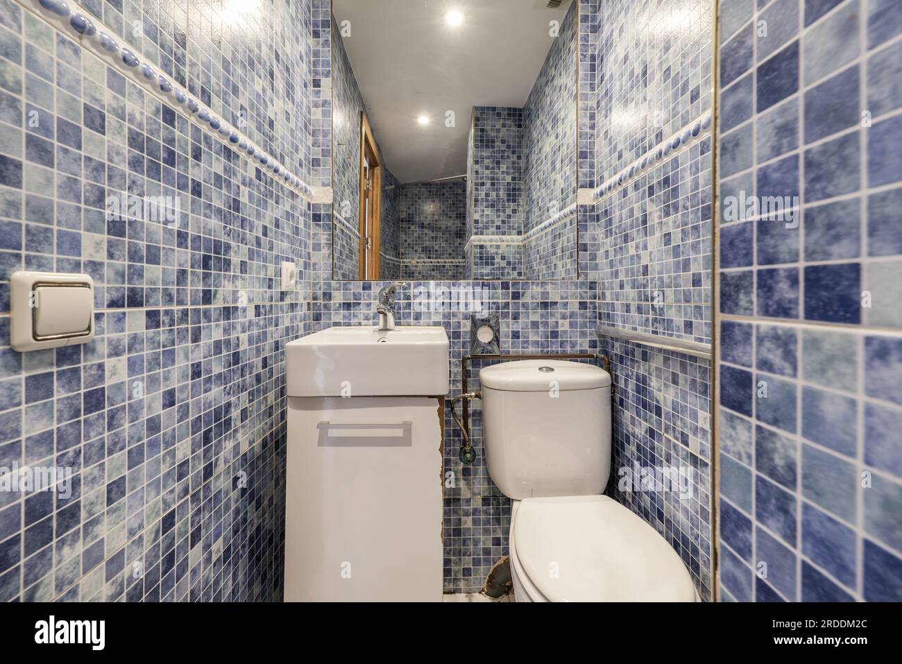 Une petite salle de bain avec un lavabo carré en porcelaine, un miroir sans cadre et des carreaux bleus ressemblant à une gressite Banque D'Images