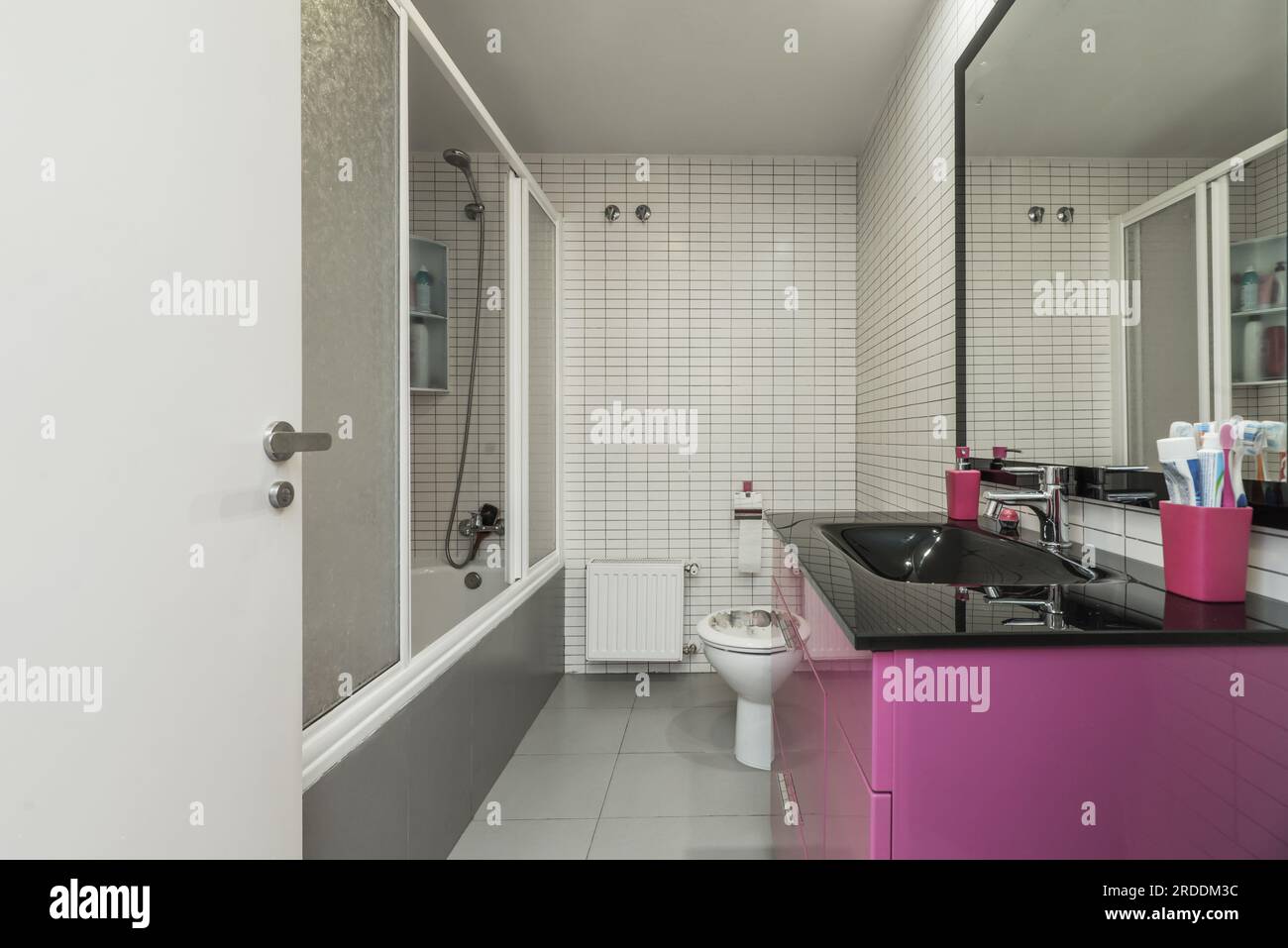Une salle de bains avec un lavabo noir brillant, armoire en bois avec tiroirs violets profonds, baignoire avec écrans, miroir encadré noir et carreaux de métro blancs Banque D'Images