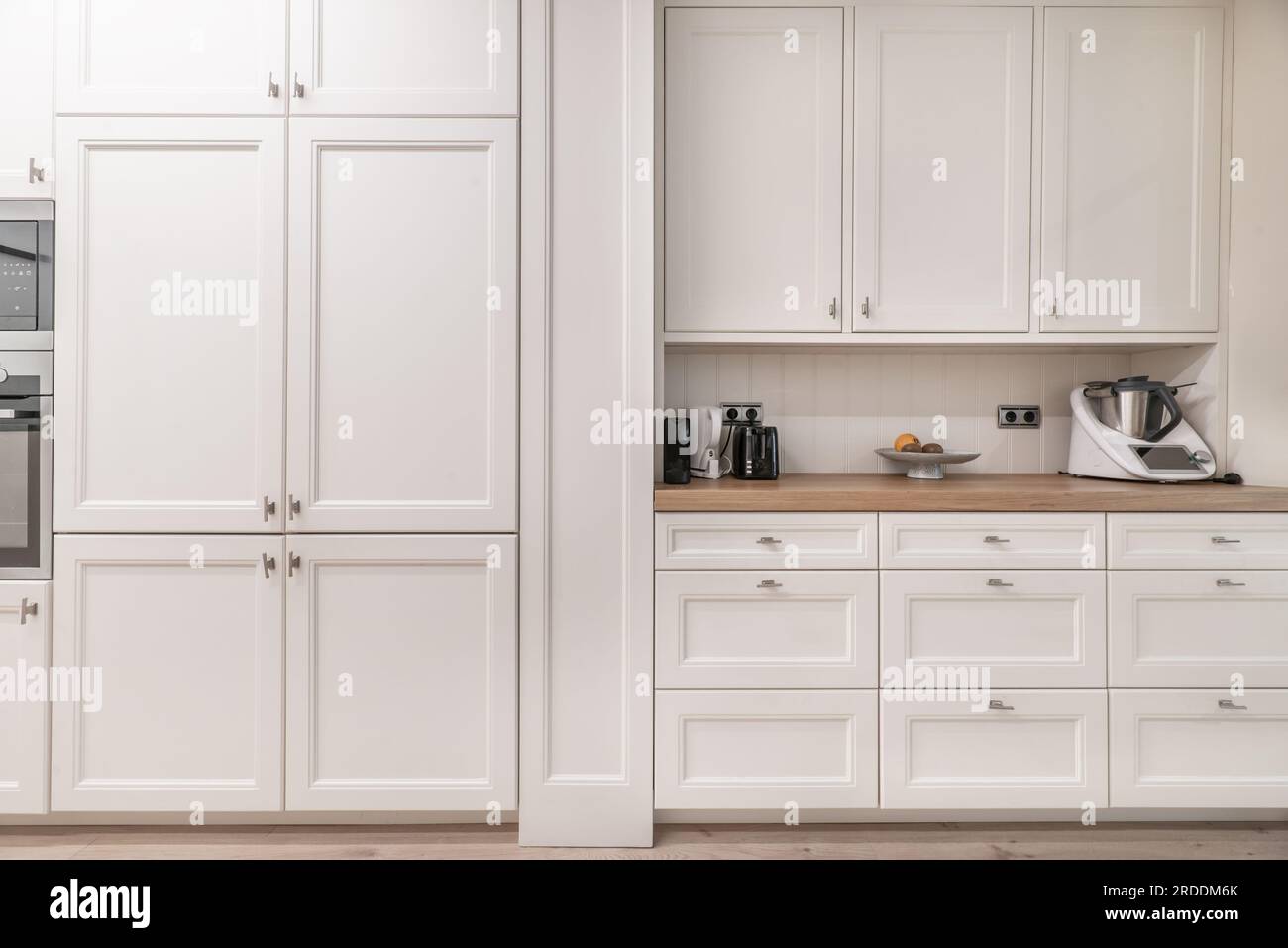 Paroi avant d'une cuisine recouverte d'armoires en bois blanc avec toutes sortes de portes, tiroirs, tiroirs et appareils électroménagers Banque D'Images