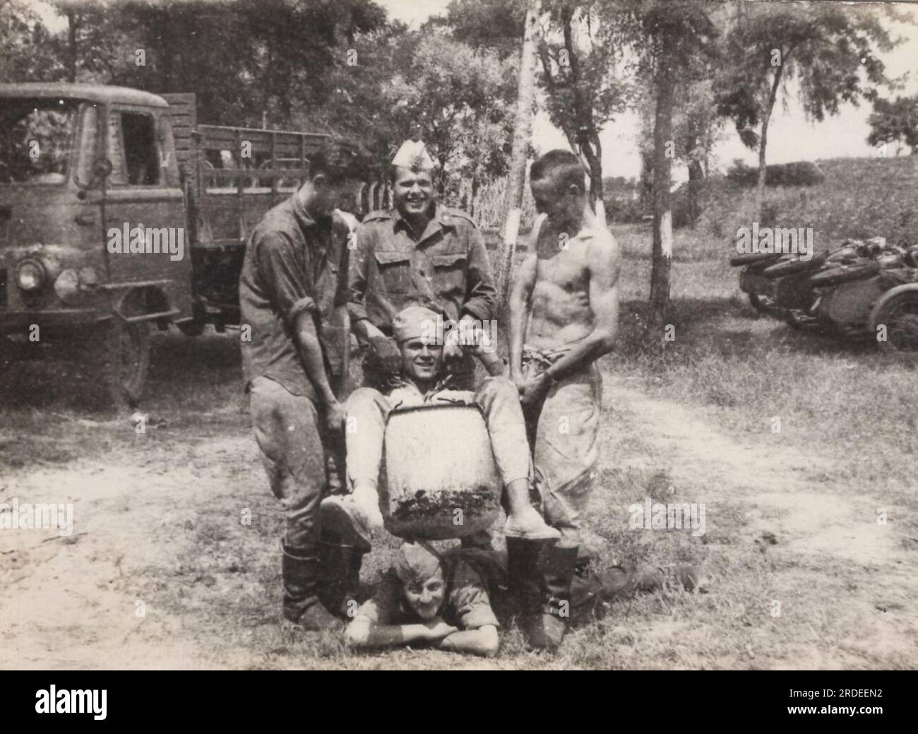 vintage drôle moment de la vie militaire des années 1960. les soldats se moquaient du dossier tenant l'un d'eux dans un sac. Camion de type soviétique à l'arrière ( camion léger ROBUR / camion Robur ) Banque D'Images