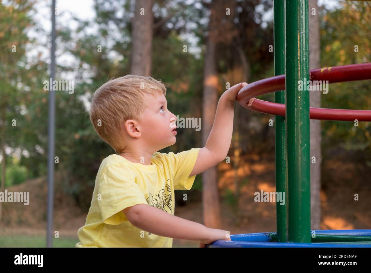 Mignon petit garçon avec les cheveux blonds grimpant et jouant dans l'aire de jeux Banque D'Images