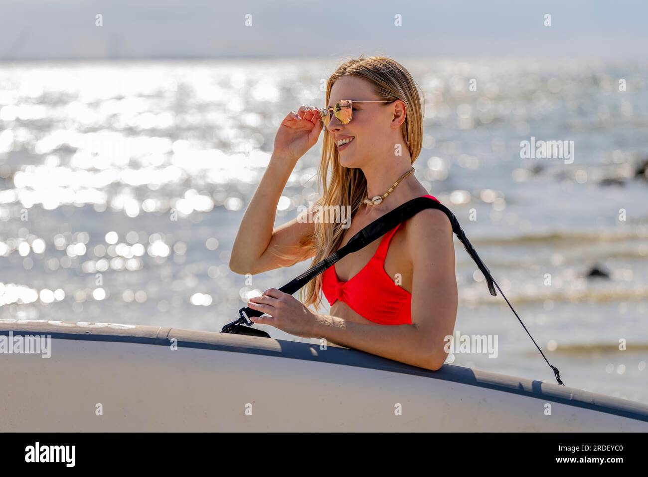 Un beau modèle blond profite d'une journée d'été tout en se préparant à surfer sur l'océan avec son paddle board Banque D'Images