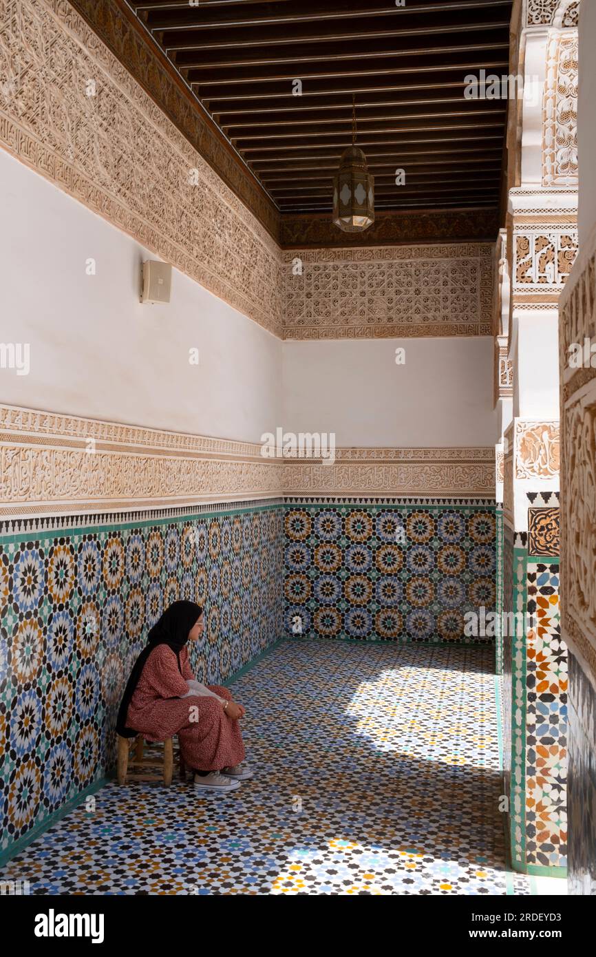 Maroc : une femme assise dans l'une des galeries entourant la cour centrale, Ben Youssef Madrasa (Medersa Ben Youssef), Médina de Marrakech, Marrakech. Le sultan de la dynastie saadienne, Abdallah al-Ghalib Billah (1517 - 1574), a construit la madrasa en 1565 (972 AH). C'était autrefois le plus grand collège islamique du Maghreb (Afrique du Nord-Ouest). Banque D'Images