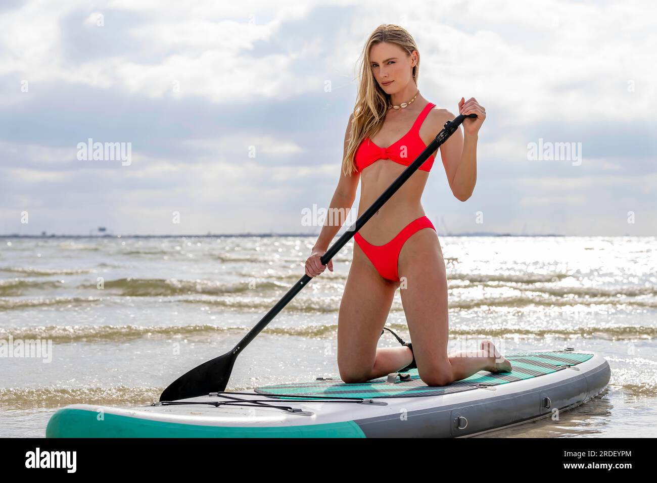 Un beau modèle blond profite d'une journée d'été tout en se préparant à surfer sur l'océan avec son paddle board Banque D'Images