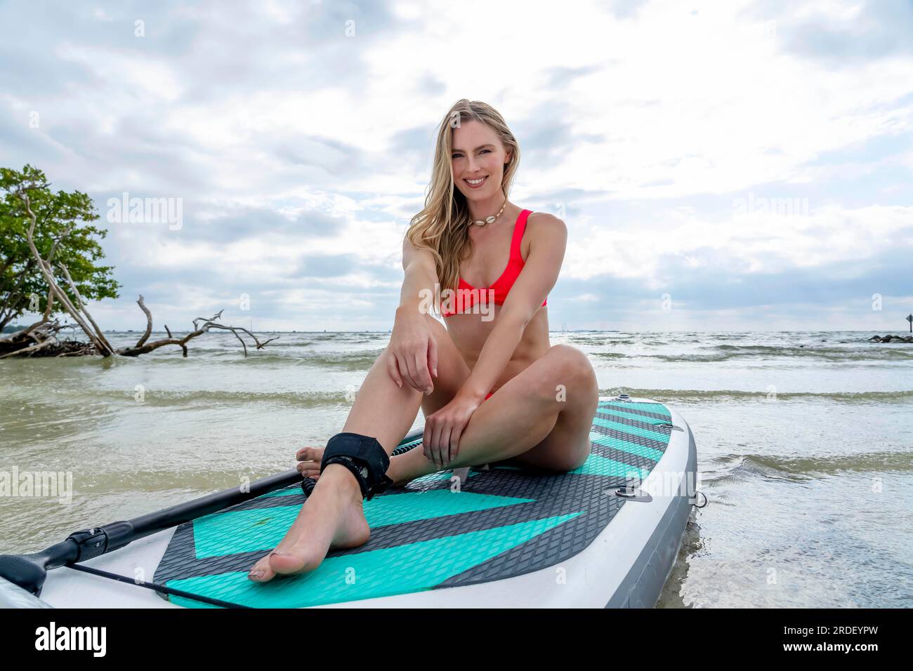 Un beau modèle blond profite d'une journée d'été tout en se préparant à surfer sur l'océan avec son paddle board Banque D'Images