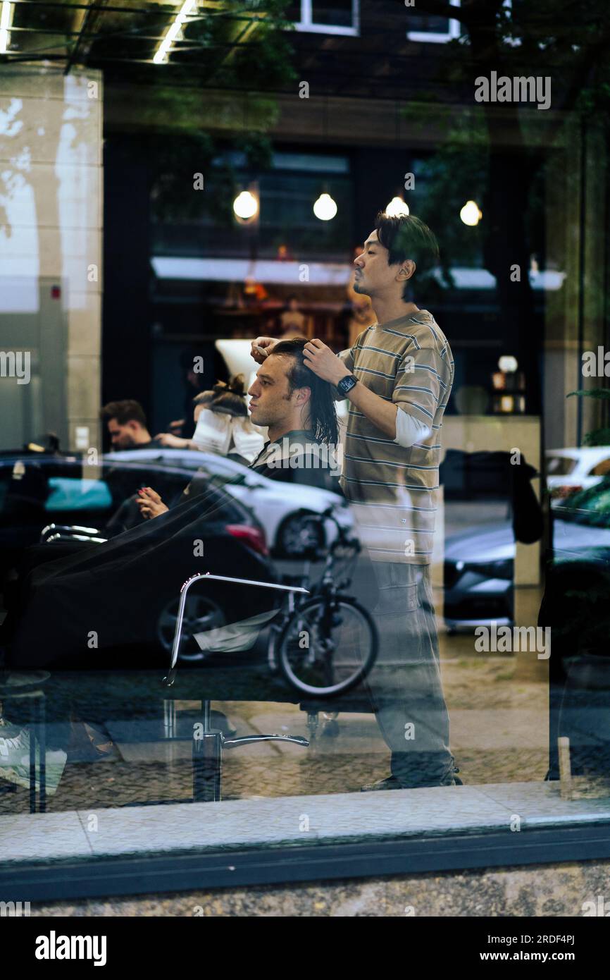 Homme dans un salon de coiffure coupant ses cheveux, abattu à travers le verre. Banque D'Images