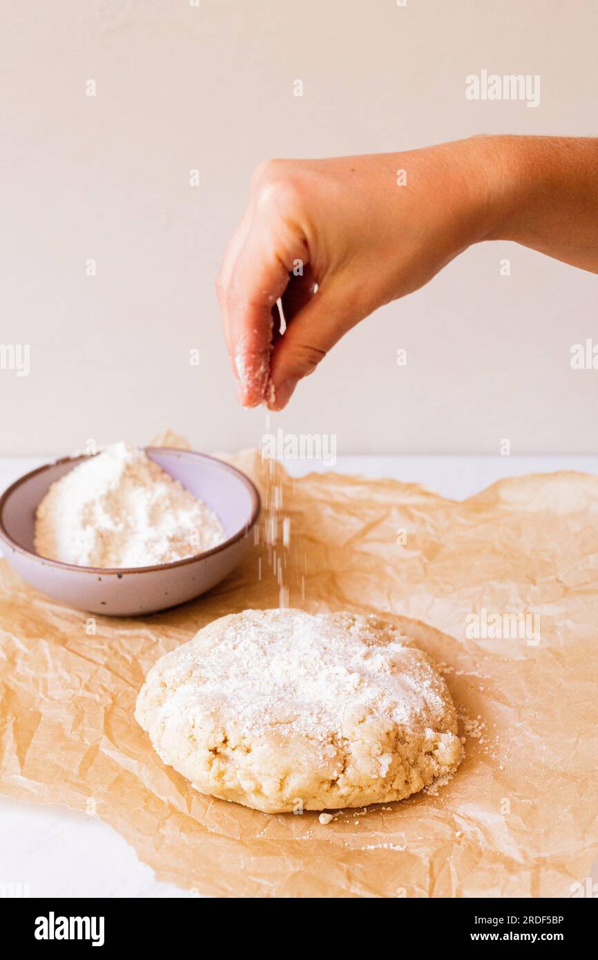 Une main saupoudrer la farine sur le dessus de la pâte posée sur du papier parchemin Banque D'Images