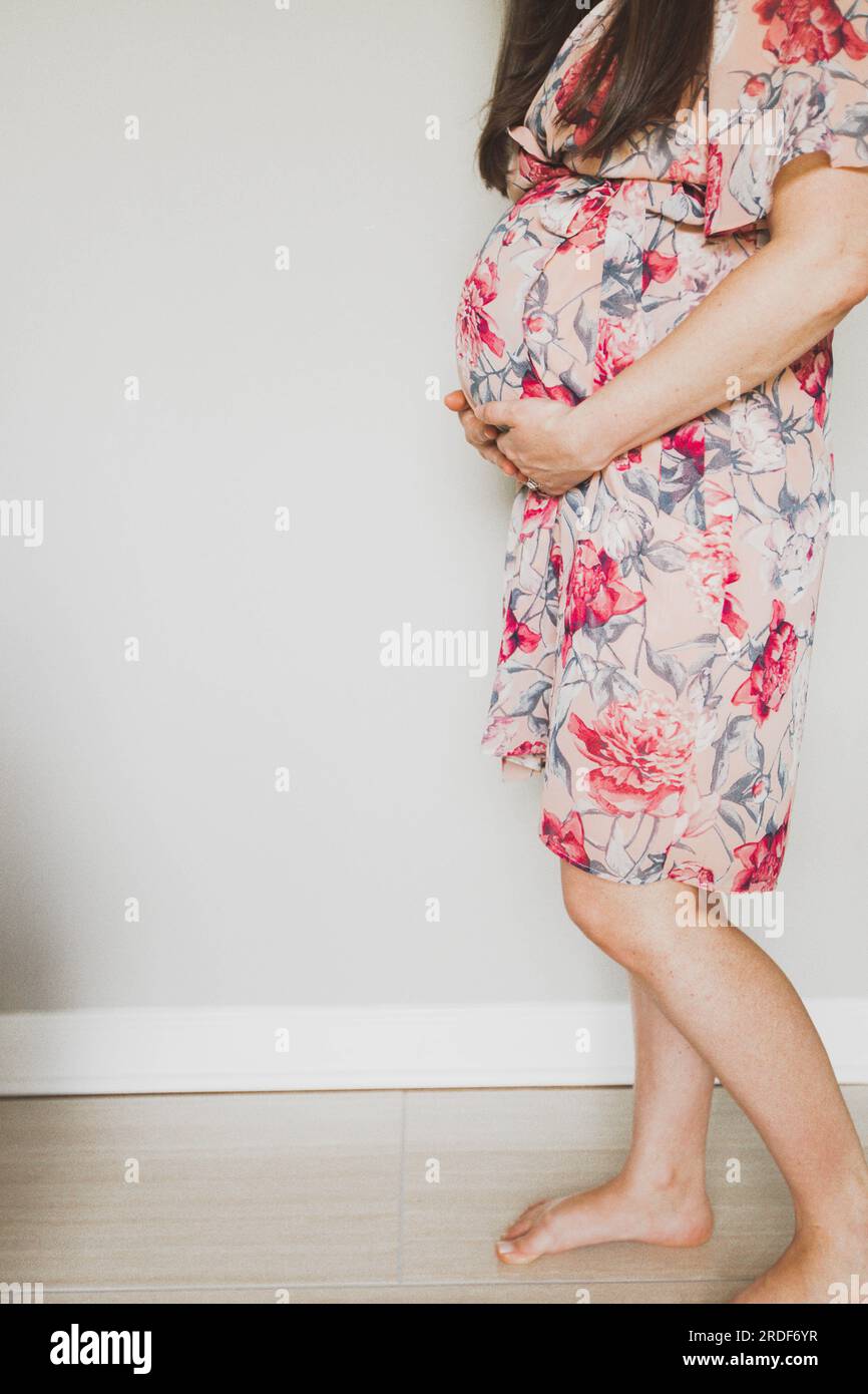 Femme enceinte avec les mains sur le ventre en robe florale Banque D'Images