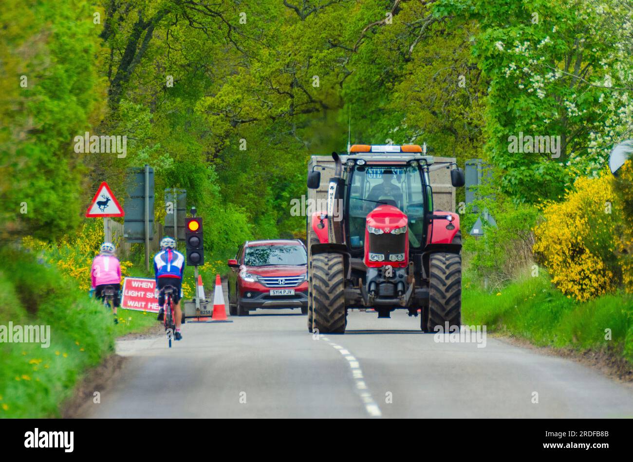 BEAULY, ÉCOSSE, Royaume-Uni - 17 mai 2022 - deux cyclistes attendent à un feu de circulation à contre-courant alors qu'un tracteur et d'autres véhicules passent près de Beauly, Inverne Banque D'Images