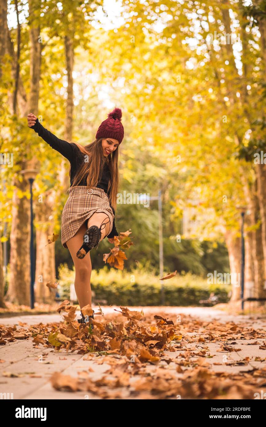 Portrait d'une femme en automne dans une forêt avec des feuilles brunes au coucher du soleil dans un parc de la ville, donnant des coups de pied aux feuilles Banque D'Images