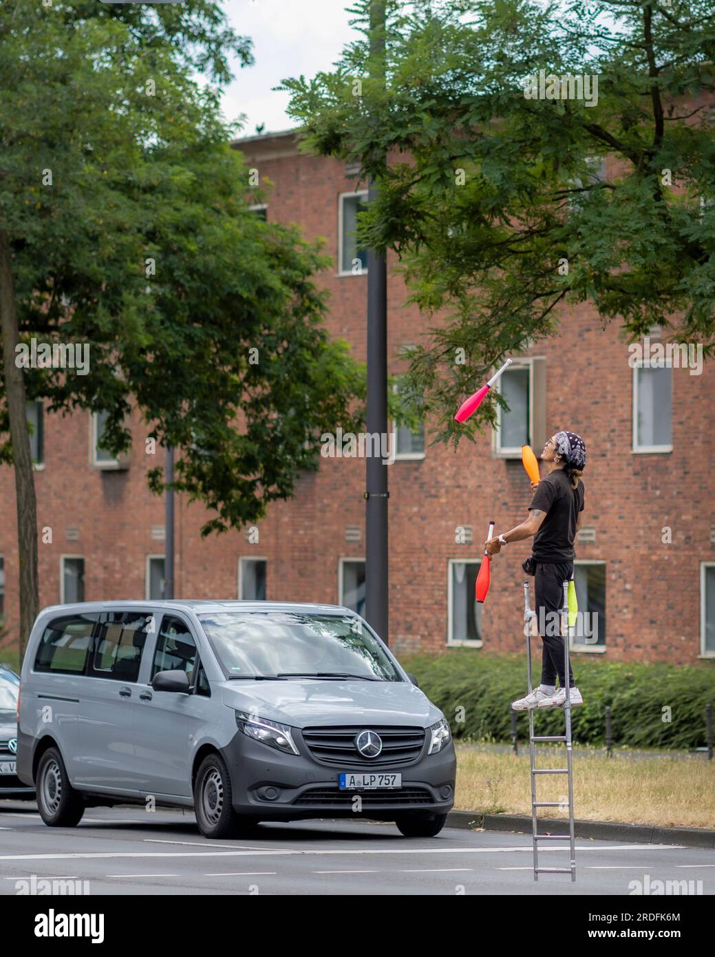 Un artiste de rue gagne sa vie en se produisant devant des conducteurs de voiture debout dans la lumière rouge. Banque D'Images