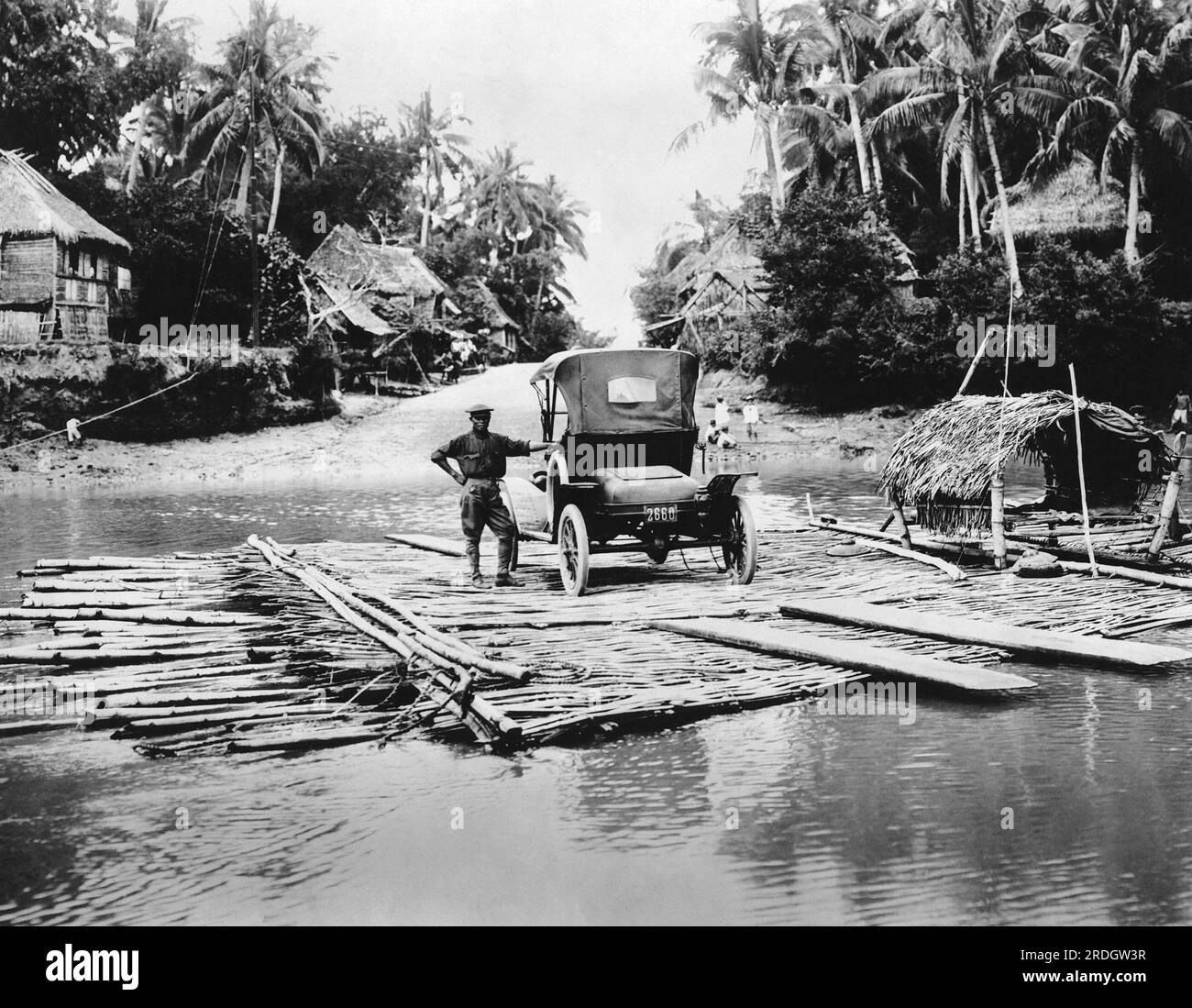 Philippines : c. 1923 Une plate-forme flottante faite de poteaux de bambou et actionnée à la main par un câble sur poulies sert de ferry pour un gué de 1915 à travers l'une des nombreuses rivières et ruisseaux dans les Phillipines. Banque D'Images