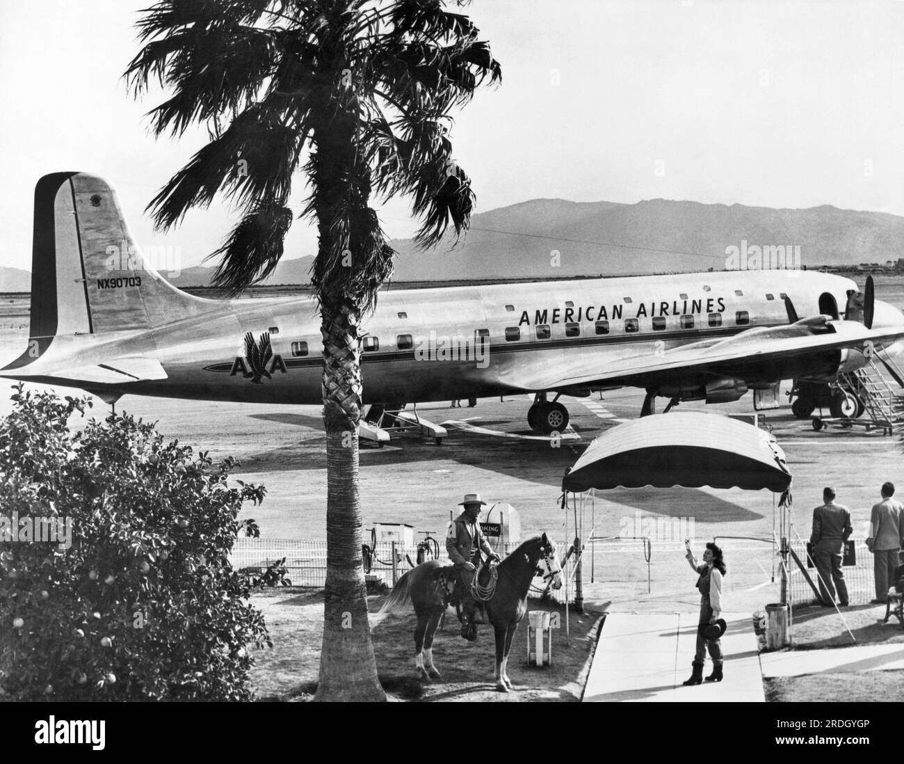 Tucson, Arizona : c. 1948 un navire amiral DC-6 d'American Airlines à l'aéroport de Tucson alors qu'une femme en tenue de cow-girl offre adieu à un cow-boy à cheval dans la zone d'embarquement. Banque D'Images