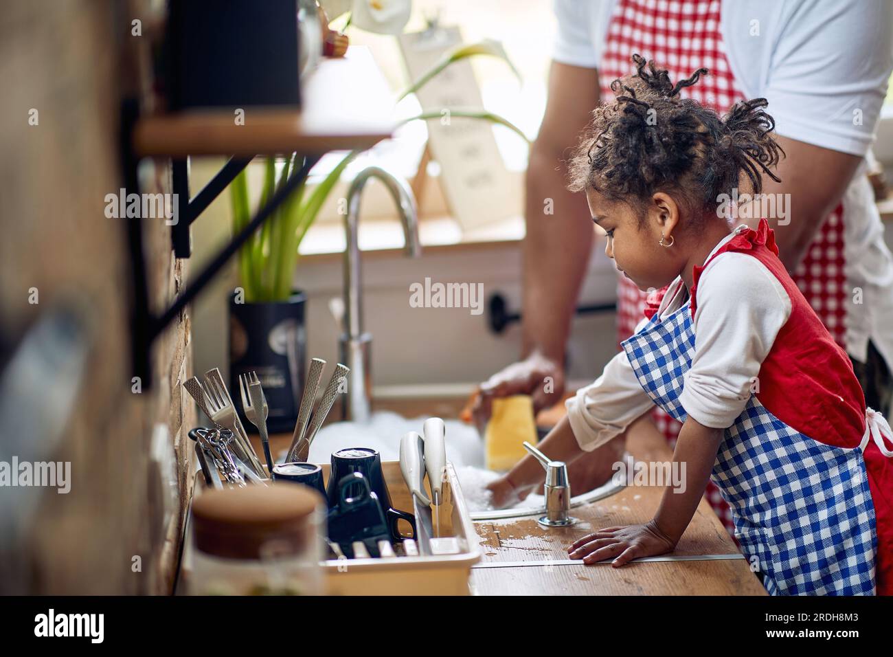 Mignonne petite fille aider son père avec la vaisselle dans une cuisine domestique, laver la vaisselle ensemble, travailler en équipe. Maison, famille, concept de style de vie Banque D'Images