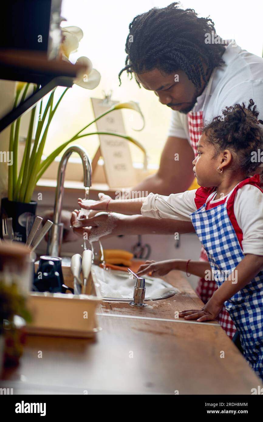 Jeune père faisant la vaisselle avec sa petite fille dans une cuisine domestique, travaillant en équipe. Maison, famille, concept de style de vie. Banque D'Images