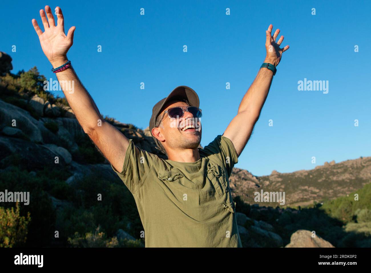 Homme vêtu de t-shirt vert militaire et casquette et lunettes de soleil profitant d'une journée dans les montagnes Banque D'Images