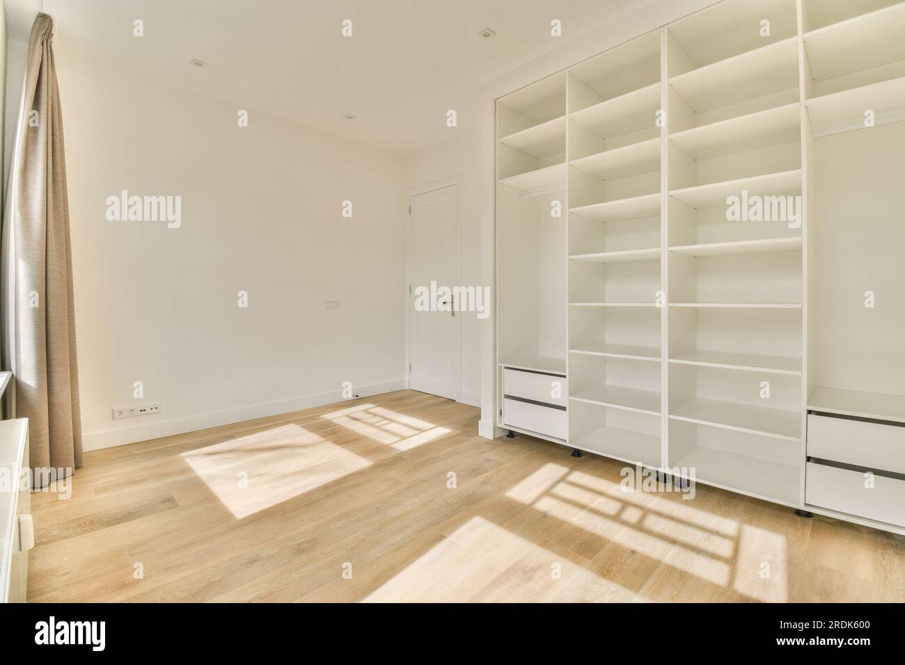 une pièce vide avec plancher en bois et bibliothèques blanches sur le mur, il y a la lumière du soleil qui brille à travers la fenêtre Banque D'Images