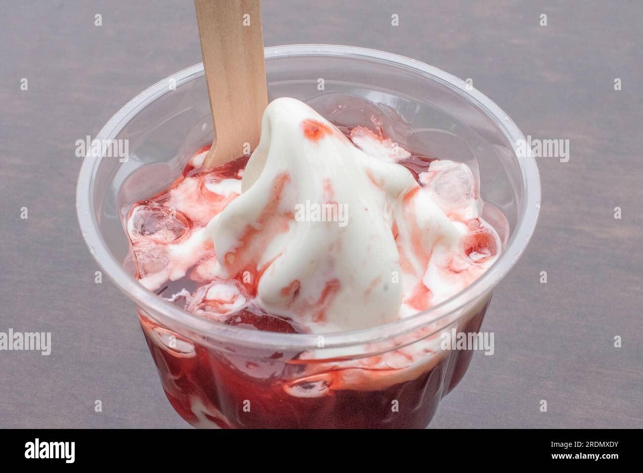 Une délicieuse crème glacée servie dans une tasse en plastique, garnie de sirop de fruits savoureux et remplie de crème glacée appétissante aux fraises. Sélectif f Banque D'Images