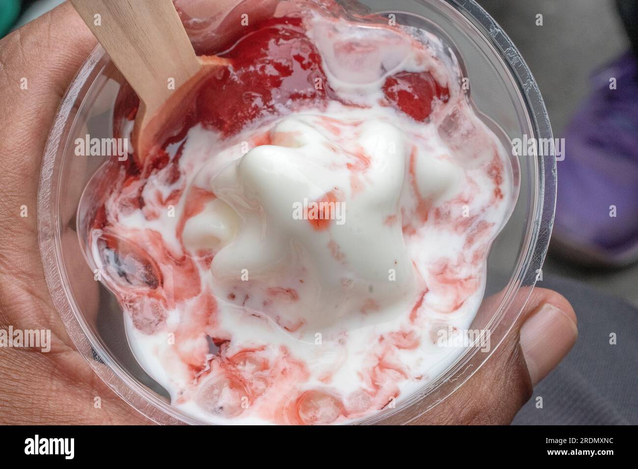 Une délicieuse crème glacée servie dans une tasse en plastique, garnie de sirop de fruits savoureux et remplie de crème glacée appétissante aux fraises. Sélectif f Banque D'Images