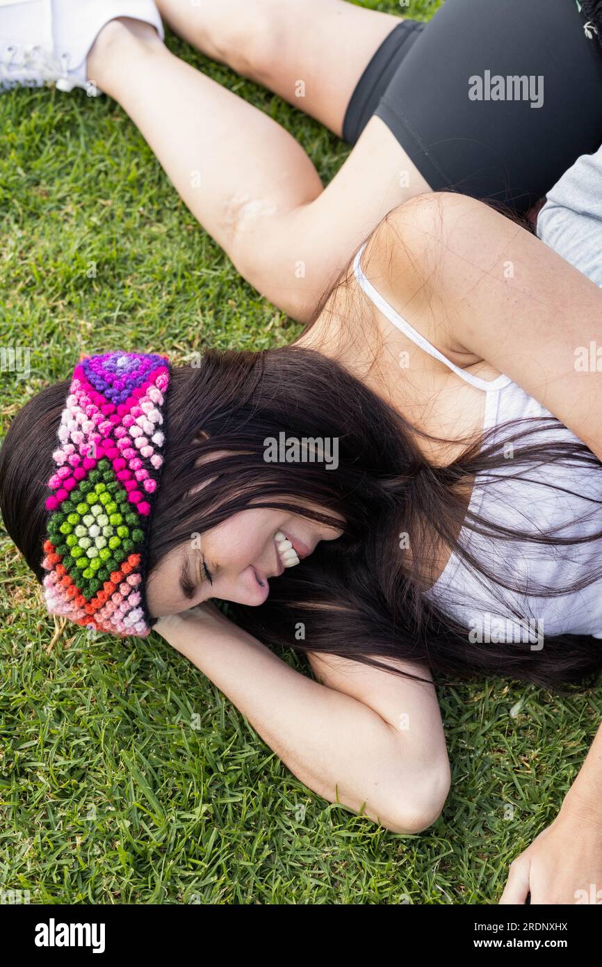 couchée sur l'herbe une jeune femme avec les cheveux raides et un bandeau coloré comme décoration, jouant et riant par une journée ensoleillée, style de vie Banque D'Images