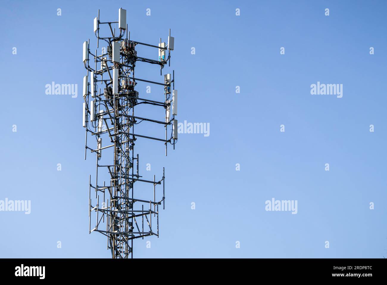 Tour cellulaire monopôle haute avec échafaudage métallique et antennes - panneaux rectangulaires gris - fond bleu clair du ciel Banque D'Images