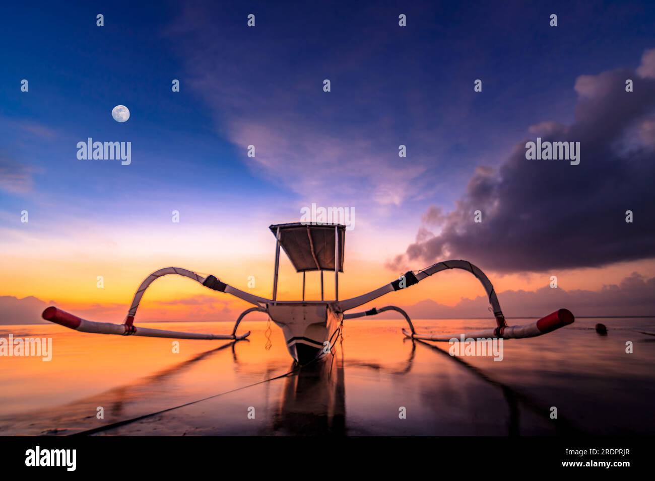 Bali Sanur, bateau de pêche traditionnel au lever du soleil. Gros plan dans l'eau peu profonde et calme avec rétro-éclairage et grand ciel. jukung Banque D'Images