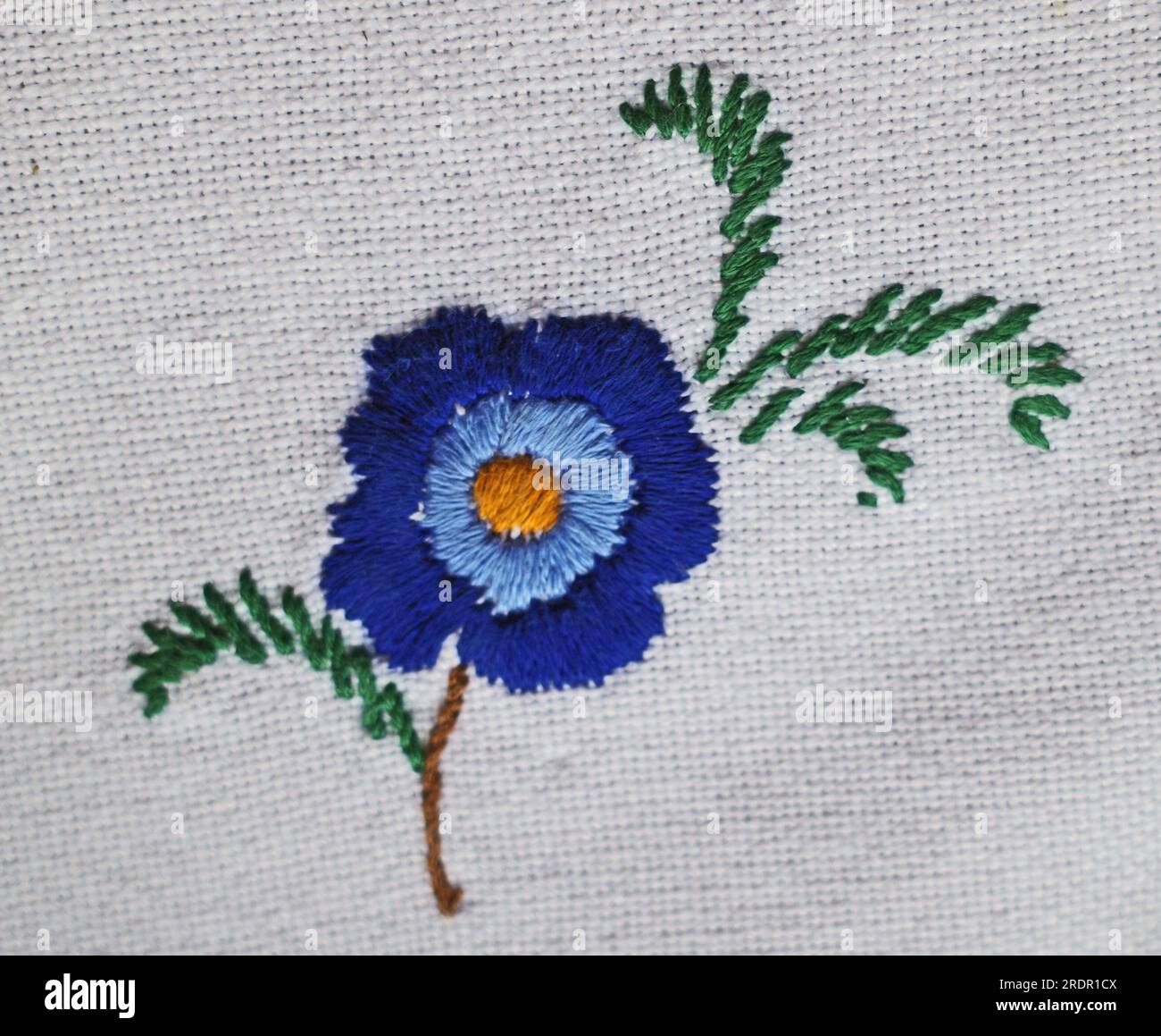 Broderie fleur bleue avec des feuilles sur fond blanc. Banque D'Images