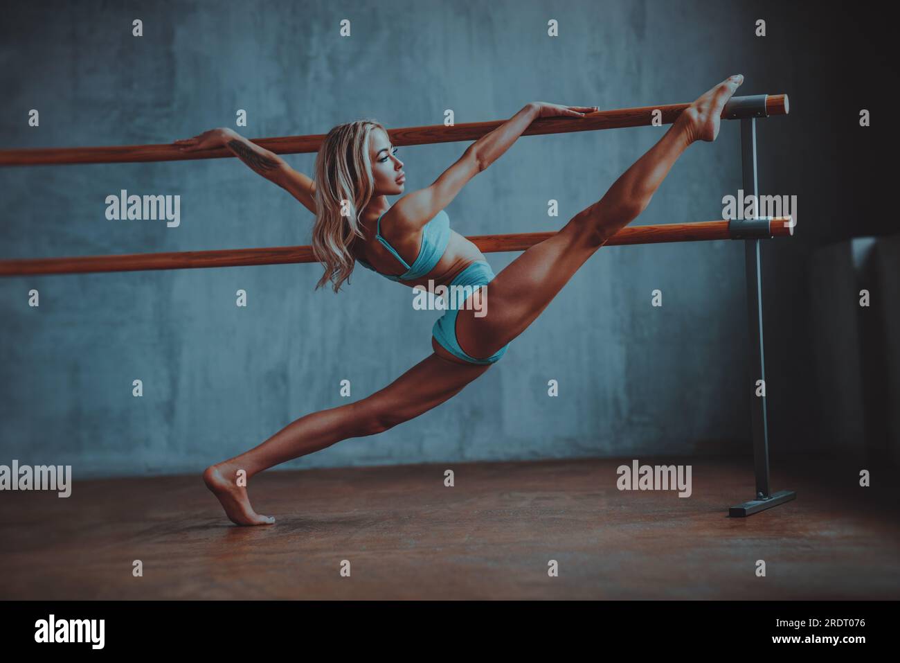 Jeune femme gymnaste s'étirant à la barre de ballet sur fond de mur, tatouage sur la main Banque D'Images