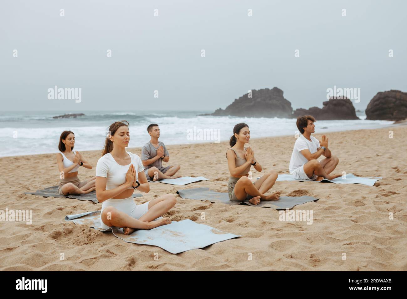 Jeunes hommes et femmes pacifiques méditant ensemble sur la plage, pratiquant le yoga en position lotus avec les yeux fermés Banque D'Images