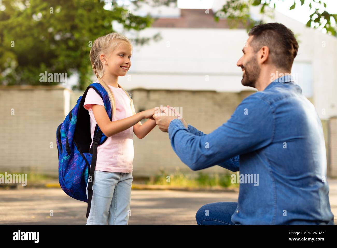 Naviguer dans de nouveaux départs. Père menant sa fille en première année, se tenant la main et parlant avec l'enfant dans la cour arrière Banque D'Images