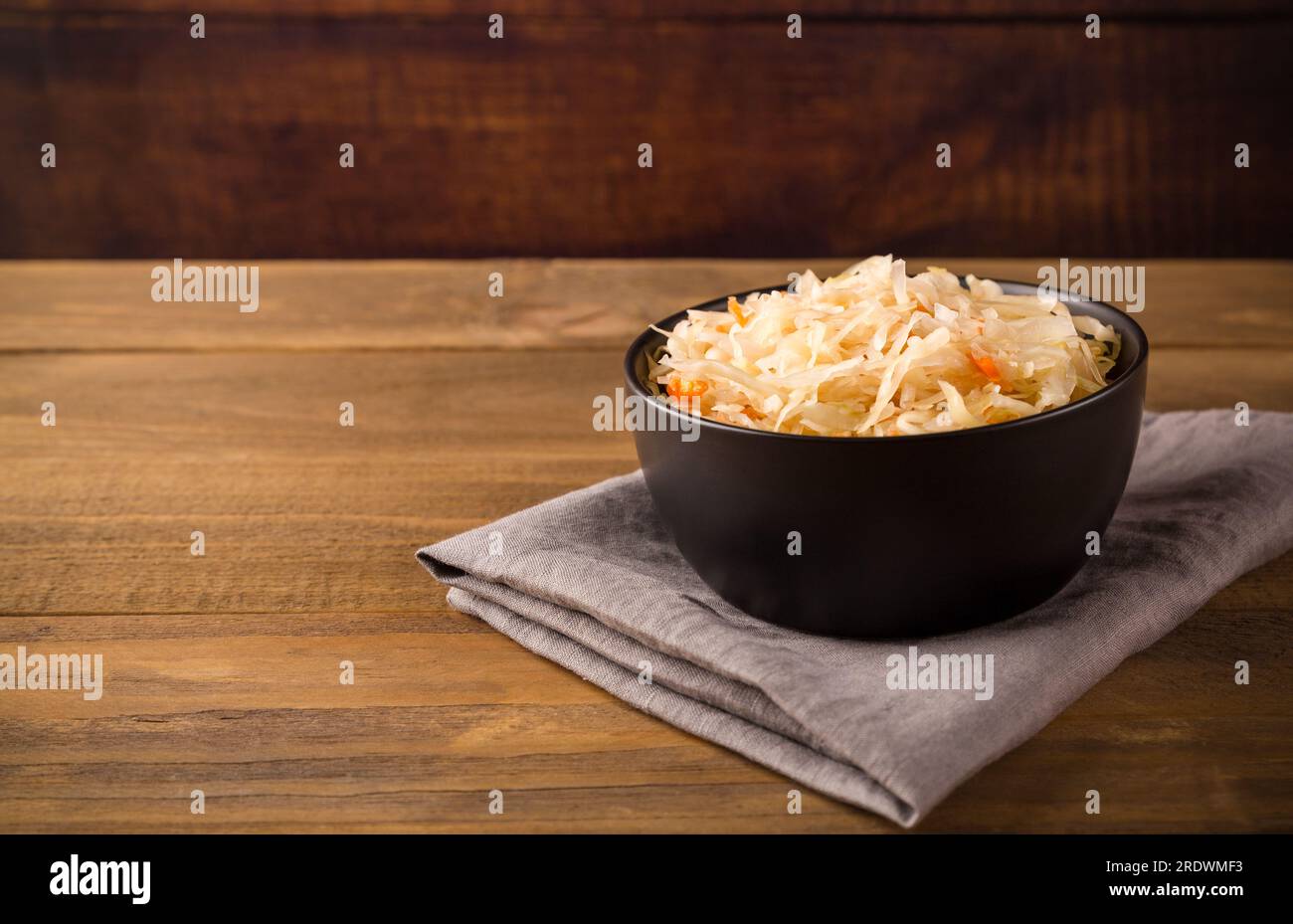 Bol noir avec choucroute aigre sur serviette grise sur fond brun en bois gros plan avec espace de copie. Banque D'Images