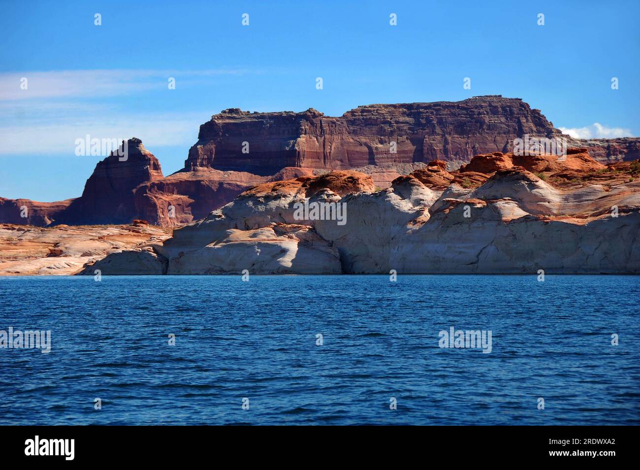 L'érosion créative laisse des collines arrondies de grès et des falaises géantes de grès accidenté. Blue Lake Powell et le ciel bleu encadrent des falaises érodées. Banque D'Images