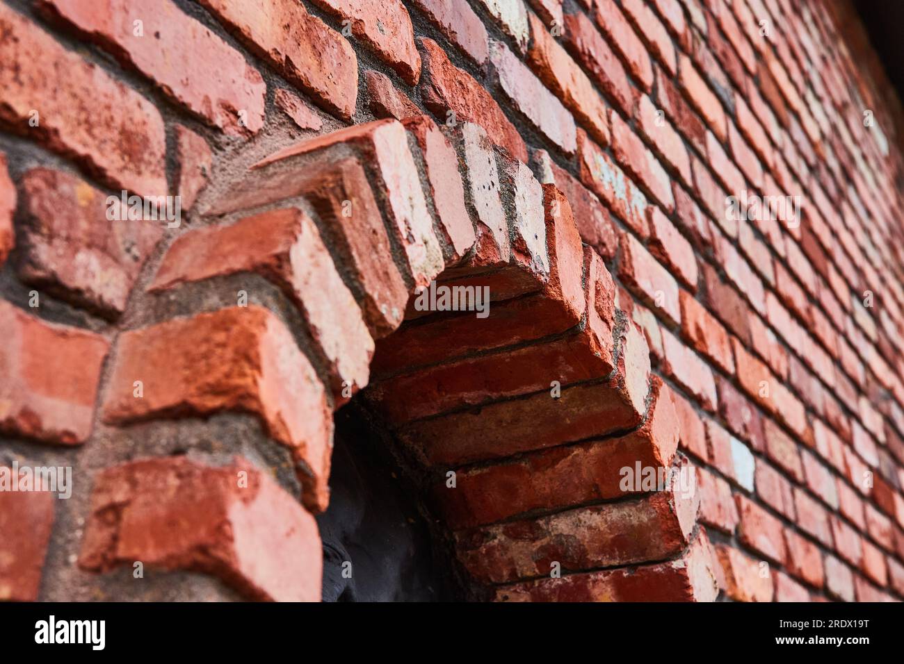Mur de briques rouges incliné avec arche circulaire saillante sur le fond et motif noir à l'intérieur du cercle Banque D'Images