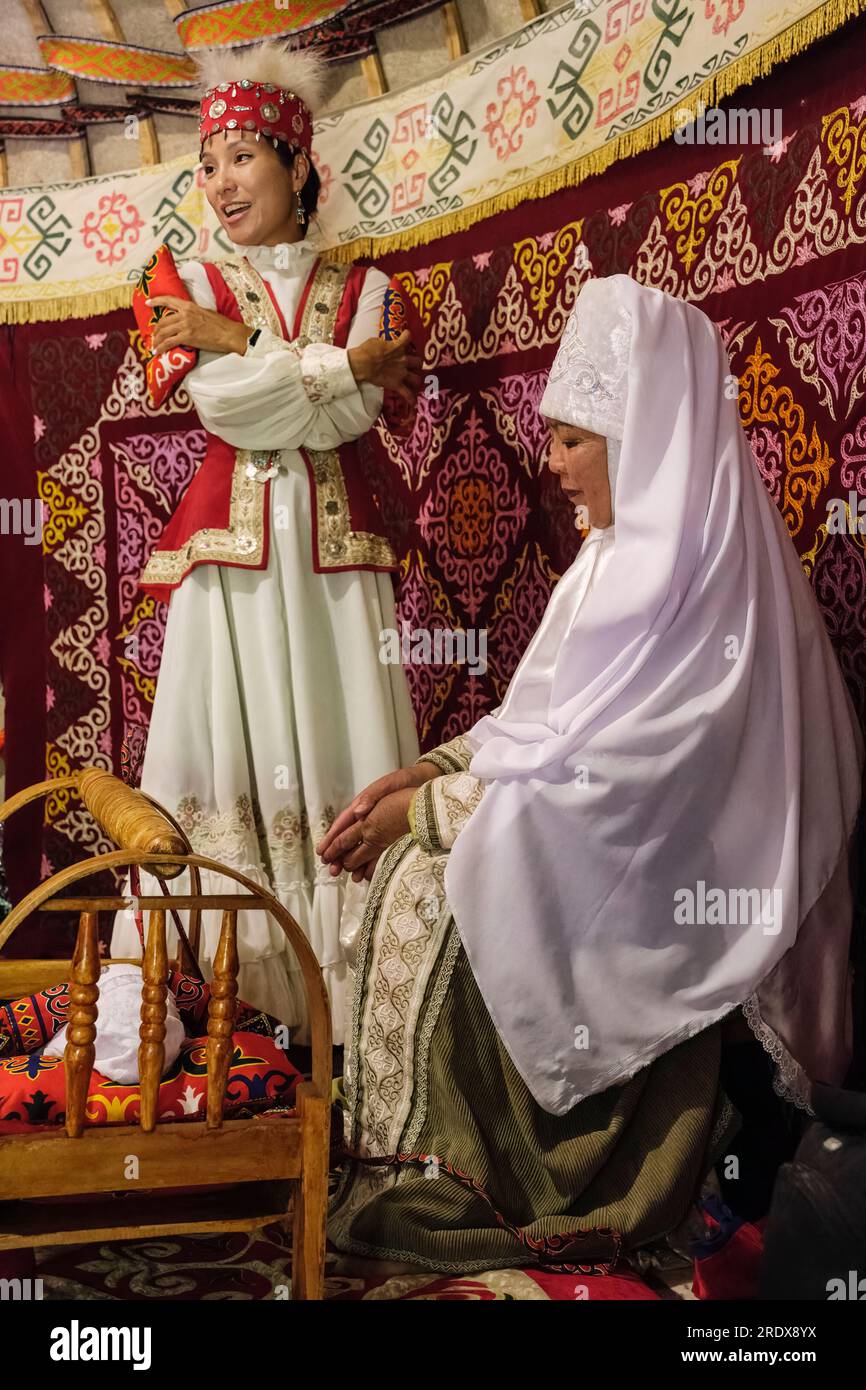 Kazakhstan, village ethno de Huns. Des femmes démontrant un berceau de bébé traditionnel à l'intérieur d'une yourte. Banque D'Images