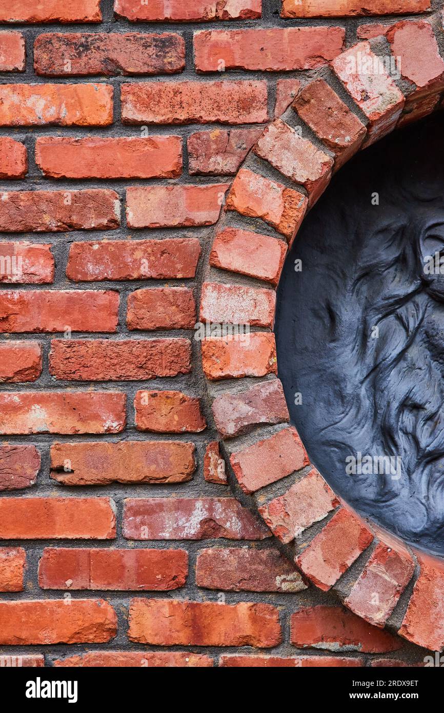 Vertical de mur de briques rouges avec demi-cercle s'ouvrant au motif noir de crinière ondulée de lions sur la droite Banque D'Images