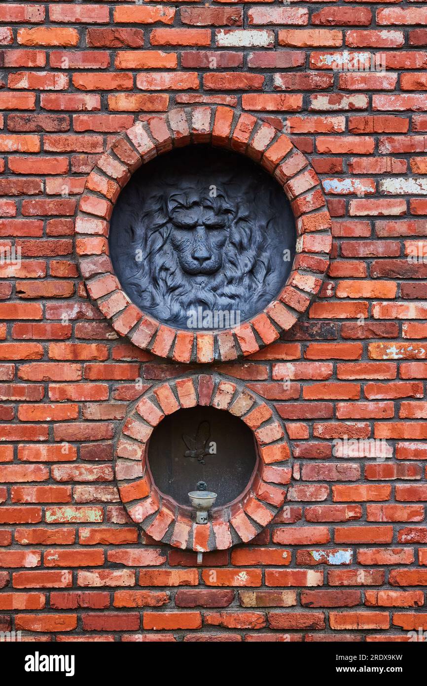 Tête de lion avec crinière et oiseau sur fontaine sur grand mur de briques rouges avec des ouvertures circulaires aux motifs Banque D'Images
