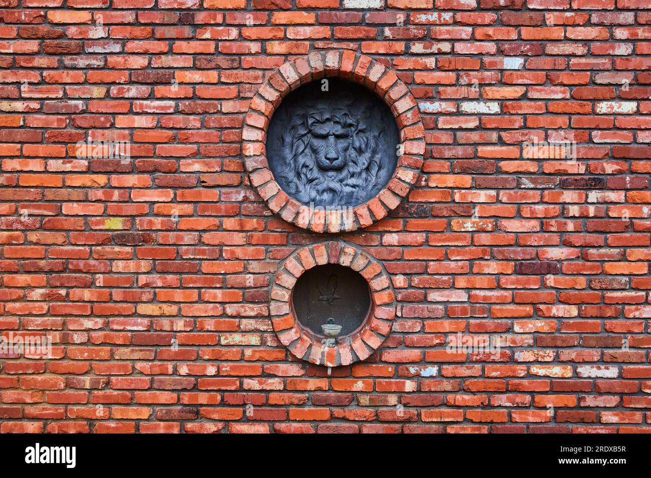 Grand mur de briques rouges avec des briques fanées à blanches, motif de tête de lion ronde et oiseau au-dessus de la fontaine d'eau Banque D'Images