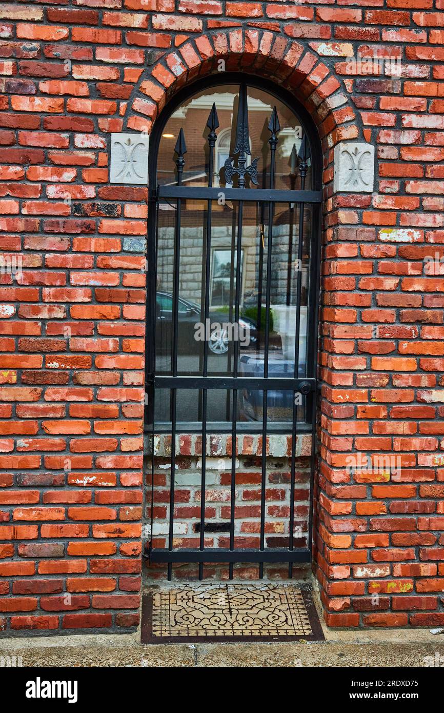 Mur de briques rouges avec portail en métal noir bloquant la porte maintenant en briques avec fenêtre et tapis de sol en métal Banque D'Images