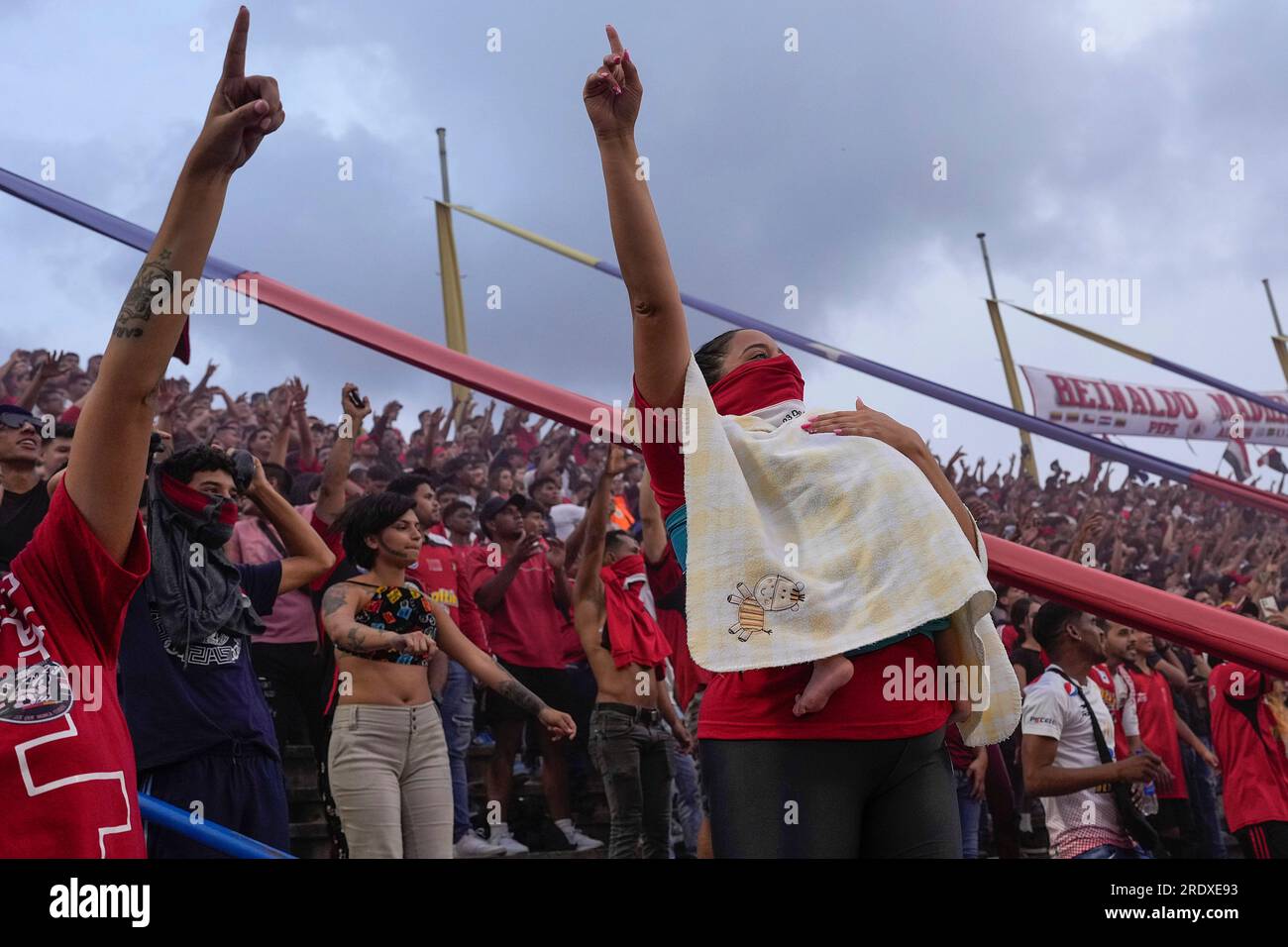 A member of the Caracas FC fan club, who call themselves The Red Demons, cheers for her team as she holds her baby during the derby soccer match against Deportivo Tachira at Estadio Olimpico in Caracas, Venezuela, Sunday, July 23, 2023. (AP Photo/Matias Delacroix) Banque D'Images