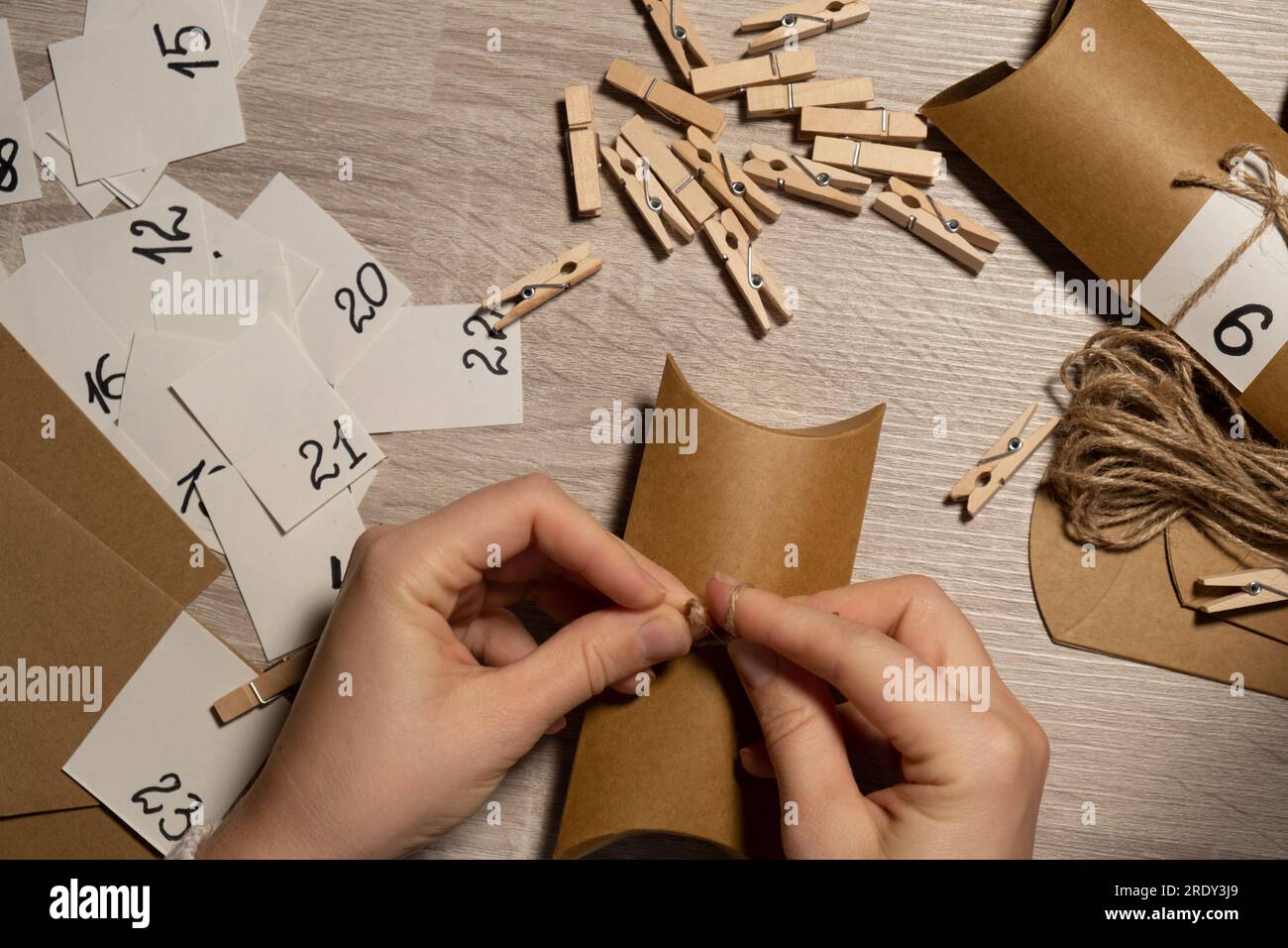 Jeune femme méconnaissable colle le numéro sur le sac d'artisanat, se fixe avec une épinglette. Femme faisant du papier kraft pour le calendrier de l'AVENT fait maison avec vos propres mains pas à pas bricolage artisanat faites-le vous-même. Préparation au concept de noël. Activités saisonnières pour les enfants vacances d'hiver en famille. Écologique cadeaux cadeaux. ouvrez le paquet tous les jours Banque D'Images